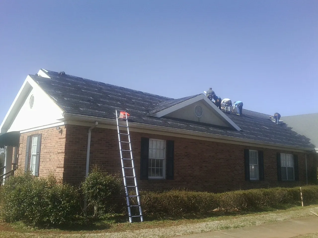 Crew tearing shingles off a brick ranch roof with a ladder set — Emergency Roof Repair work by our crew in Topton
