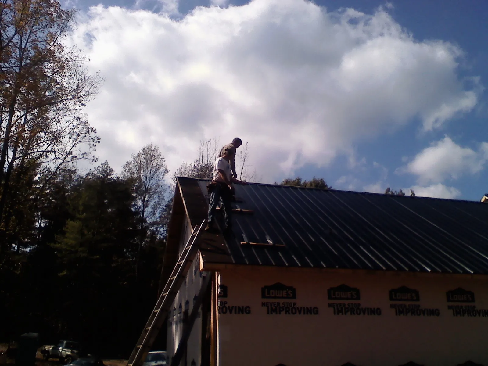 Roofer fastening dark metal panels high against a cloudy sky, from a Roof Inspection job in Topton