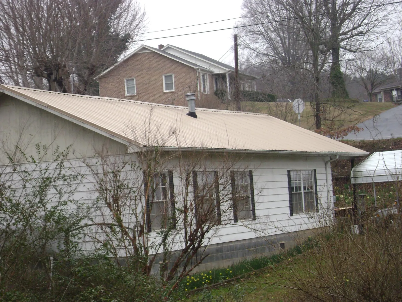 Tan metal roof on a white sided house set into a hillside — Commercial Roofing by Roofing Brothers in Topton